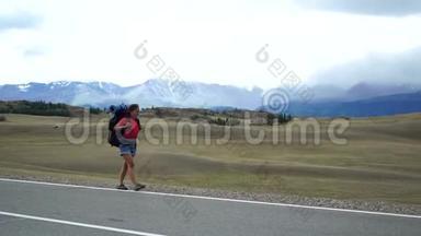 旅行者女孩带着背包走在山路的一侧。 背景中有雪山