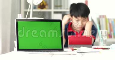 笔记本电脑上的绿色屏幕和背景平板电脑上的亚洲男孩