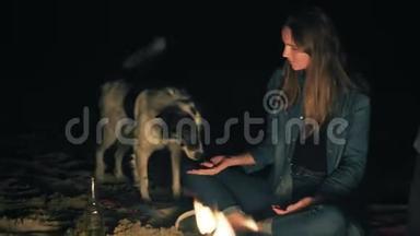 可爱的白种人女人在深夜坐在篝火旁喂可爱的狗。 亲密的女人`她的手