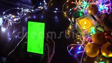 使用智能手机手在黑色背景桌子与彩色灯，圣诞节新年作文。 智能手机游戏