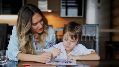 美丽的妈妈帮助她的儿子用彩色铅笔画图像。 帮助培养孩子`想象力。