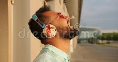 穿着时尚粉色太阳镜和耳机的放松的美国黑人男子正在机场航站楼附近大笑。 4k个镜头