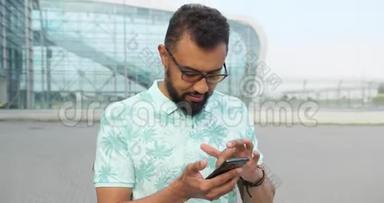 自信迷人的戴眼镜的非洲男人正在玻璃建筑附近的<strong>手机</strong>上浏览和发短信。 <strong>旋转</strong>