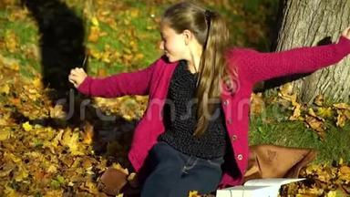 一个年轻漂亮的十几岁的女孩坐在秋天森林的一棵树下读一本书。 她做梦。 女孩很安详