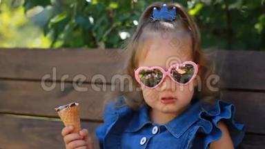 一个阳光明媚的夏日，戴太阳镜的小女孩正坐在公园的长凳上吃冰淇淋。