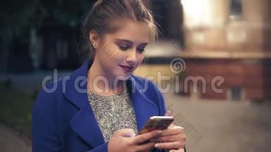 年轻迷人的女人晚上在城里用智能手机。 漂亮的女孩在户外的智能手机上发短信。 旅游女孩
