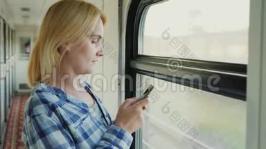 一个年轻的高加索女人站在火车车厢的窗边。 会使用智能手机。 总是上网