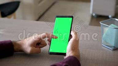 男人的手在智能<strong>手机</strong>上滚动，绿色屏幕色度<strong>模拟</strong>在他的办公桌上