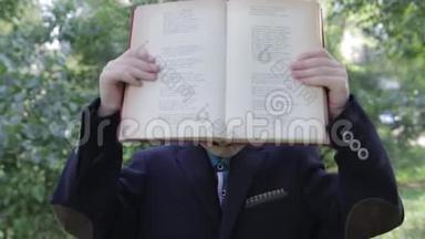 一个手里拿着书的男孩在玩他的脸。 这个男孩从书后面看起来很有趣。 穿夹克的男孩。