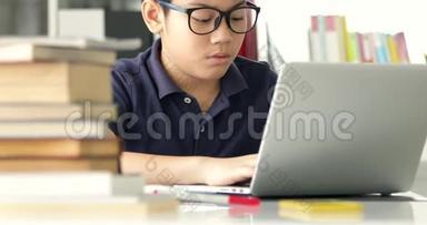 亚洲十几岁男孩提防眼镜，在家里用笔记本电脑，可爱的男孩认真地做作业。
