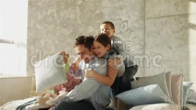 一位年轻的父亲和三个孩子抱着坐在床上。 <strong>快乐</strong>的父亲。 <strong>父亲节</strong>`