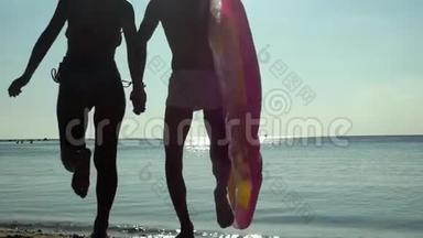 年轻快乐的夫妇牵着手，拿着床垫跑到海里，在床垫上在海里游泳。 慢动作