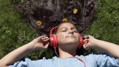 迷人的女孩，留着长长的黑发躺在公园的草地上，听着耳机上的音乐。慢动作。 高清高清