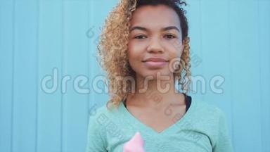 年轻<strong>的</strong>非洲女孩在蓝墙背景下吃粉色融化冰淇淋