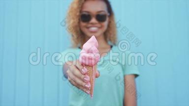 年轻的非洲女孩在蓝墙背景下吃粉色融化冰淇淋