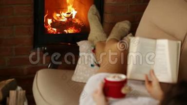 女人在炉火旁放松，喝上一杯热饮料和一本<strong>好书</strong>-专注于火焰