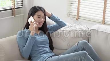 美丽的年轻亚洲女人微笑着躺在沙发上放松，女孩坐在沙发上用手机聊天享受