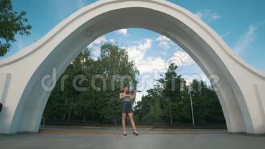 迷人的女人站在拱门下拉着小提琴在公园前面