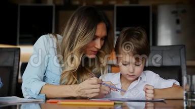 美丽的<strong>妈妈帮</strong>助她的儿子用彩色铅笔画图像。 <strong>帮</strong>助培养孩子`想象力。
