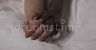 恋爱中的多民族夫妇躺在床上。 快关门。 男人的手躺在床上，女人的手在抚摸它