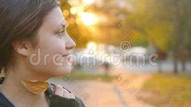 一位可爱的年轻女子在日落时在公园里欣赏秋天的肖像。 布鲁内特在秋天公园的背景