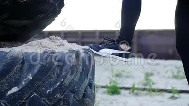 特写镜头，女人`双腿穿着黑白运动鞋跳上一个装满沙子的大型拖拉机车轮.. 女运动员表演