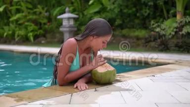 游泳运动员浑身湿透，身材苗条，手肘撑在游泳池边，喝着椰子鸡尾酒