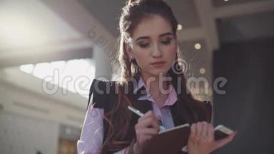 穿着粉红色衬衫和黑色无袖上衣的年轻快乐女子注意到她笔记本上的一些信息并分享