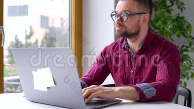 戴眼镜<strong>的大胡子男人</strong>坐在家里<strong>的</strong>办公室里用笔记本电脑工作