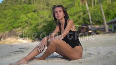 在热带森林的背景下，一位身穿<strong>黑色比基尼</strong>、坐在沙滩上的快乐年轻女子特写视频