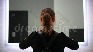 可爱的金发女人穿着黑色衬衫，系着皮带。 站在<strong>浅灰色背景</strong>上看着镜子。
