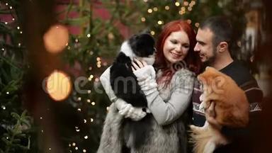 年轻夫妇在圣诞节的时候在户外玩。 他们抱着可爱的狗。 新年快乐概念。