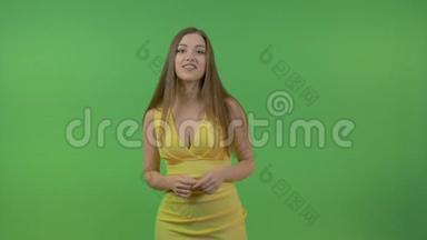 一位穿着黄色连衣裙和长发的年轻美女，问了一个问题，<strong>点击屏幕</strong>。 在绿色的背景上。