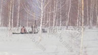 两个人骑着一辆小型雪车在冬天的森林里穿行，拖车在树林间移动