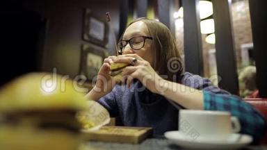 漂亮的女人在咖啡馆里吃无味的汉堡和薯条，感觉很糟糕。 戴眼镜的年轻女孩很失望