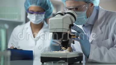 研究人员在显微镜下观察样品，助理记录，实验室