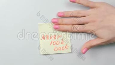 特写女人`双手贴着黄色的贴纸纸，上面写着永不回头的话。