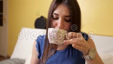 一个穿着蓝色西装的年轻女孩坐在沙发上，喝着茶想着什么。 茶饮