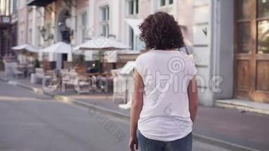 城市街上一个穿着白色t恤，蓝色牛仔裤和白色运动鞋的女人的后景。 你的腿