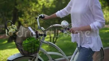 女人的近景`她手里拿着一辆城市自行车的车把，手里拿着一个花篮和一本书。 女人享受着
