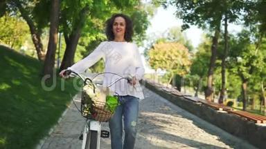 穿着白色T恤和蓝色牛仔裤的迷人女人微笑着，手里拿着她的城市自行车`带着鲜花的车把