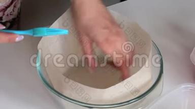 一位女士用食品纸放置一个玻璃烤盘，并用油润滑。 做蛋糕。
