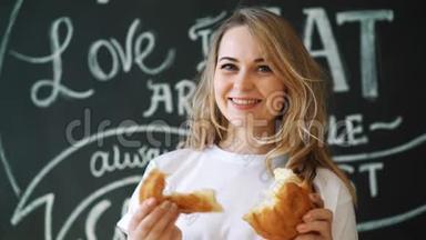 厨房里年轻漂亮的女孩坐在一张桌子旁，拿着一条面包，看着相机，微笑着。 一幅肖像画