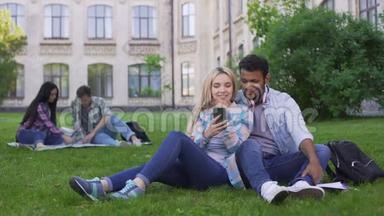 可爱的几个学生坐在<strong>草坪</strong>上看智能手机上的<strong>视频</strong>