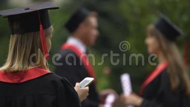 穿着学术服装和戴毕业帽的金发女孩在智能手机<strong>上上</strong>网