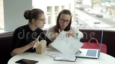两个年轻的商业女孩坐在咖啡馆里，吃<strong>中国</strong>面条，讨论商业<strong>发展</strong>。 工作。 吃东西