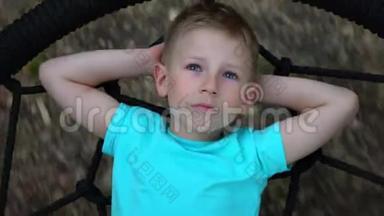 蓝眼睛的五岁男孩躺在一个圆秋千上，双手仰起头，抬头望着天空，