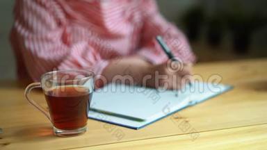 一个女孩在工作时喝茶，坐在桌子旁，一个透明的茶杯。