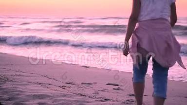 一个穿着蓝色牛仔裤和系在腰带上的粉红色夹克的女孩来到大海