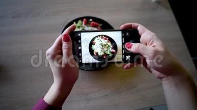 餐馆里的年轻女子用手机相机制作食物照片。 女人做沙拉的照片